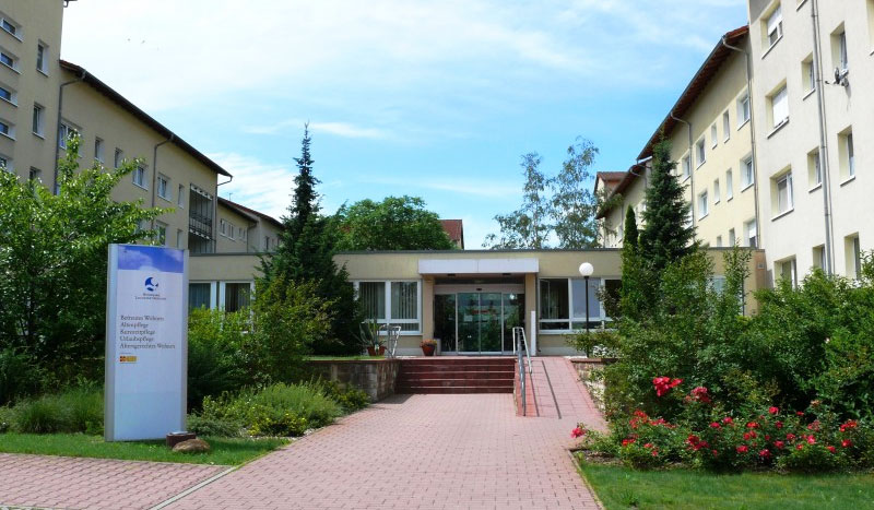 Einladender Haupteingang des Wohnparks mit Vorplatz, Rosenbeeten und Rampe